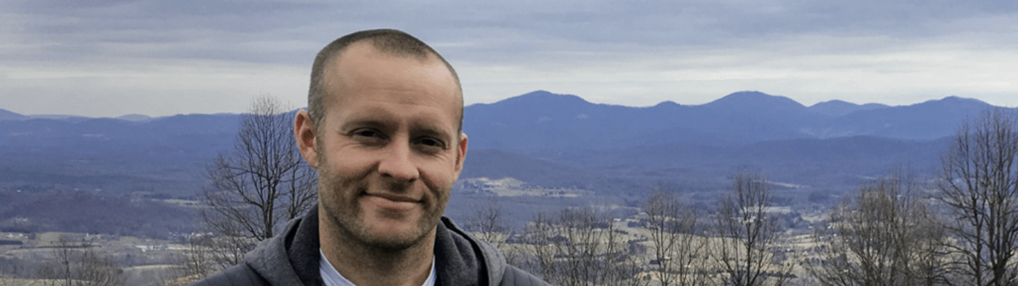 Mann vor bergiger Landschaft mit bewaldeten Hügeln im Hintergrund